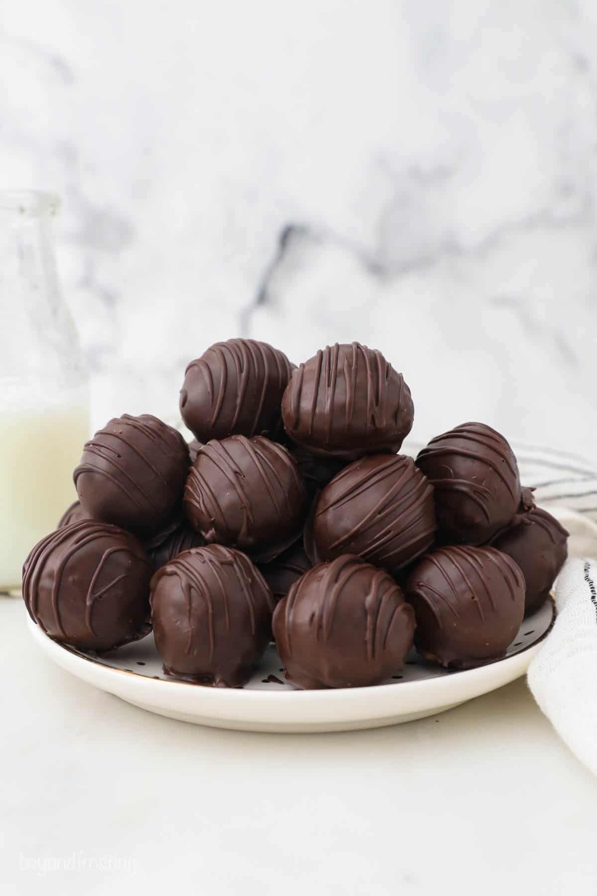 A plate piled high with peanut butter balls decorated with a dark chocolate drizzle