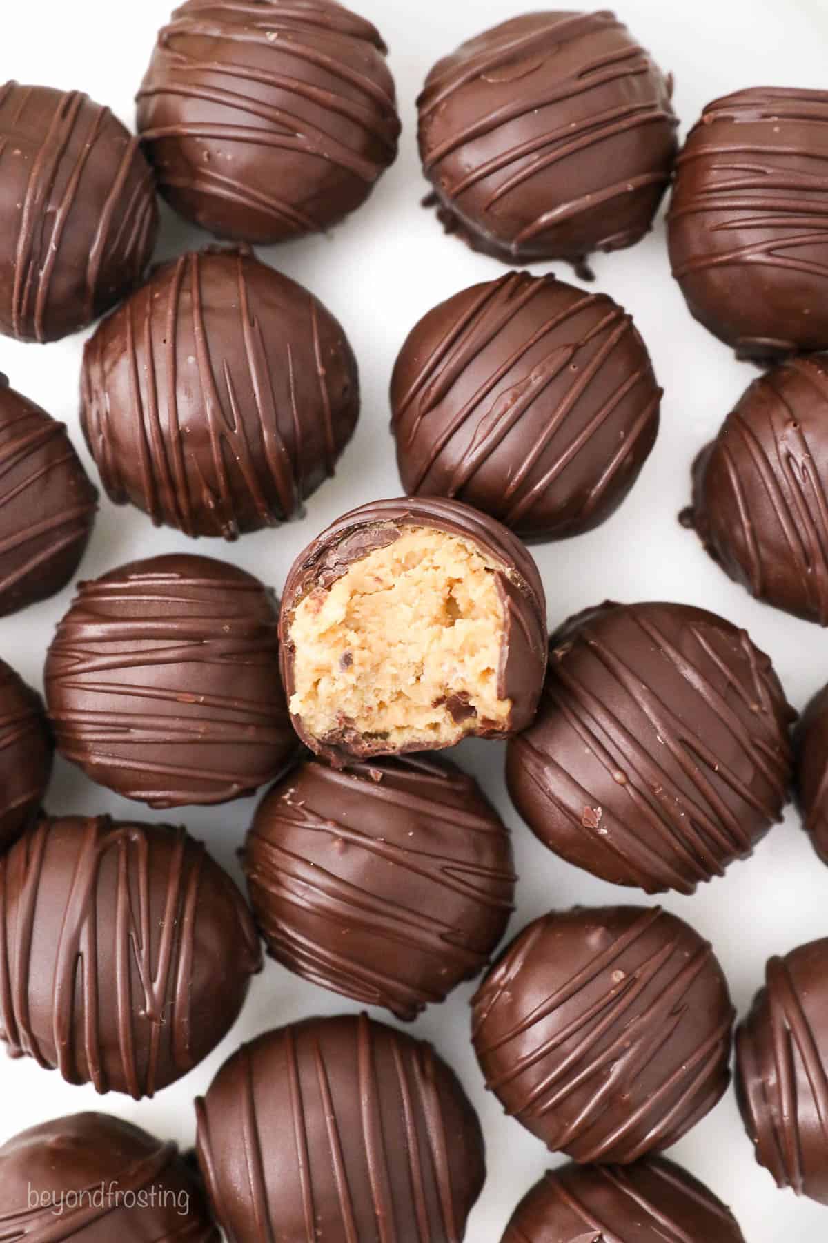 A bunch of peanut butter truffles on a white surface with a bite taken out of the one in the middle