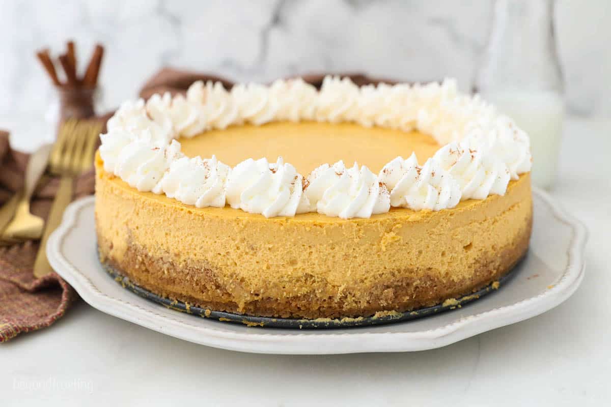 A white serving plate on a countertop containing a homemade pumpkin spice cheesecake