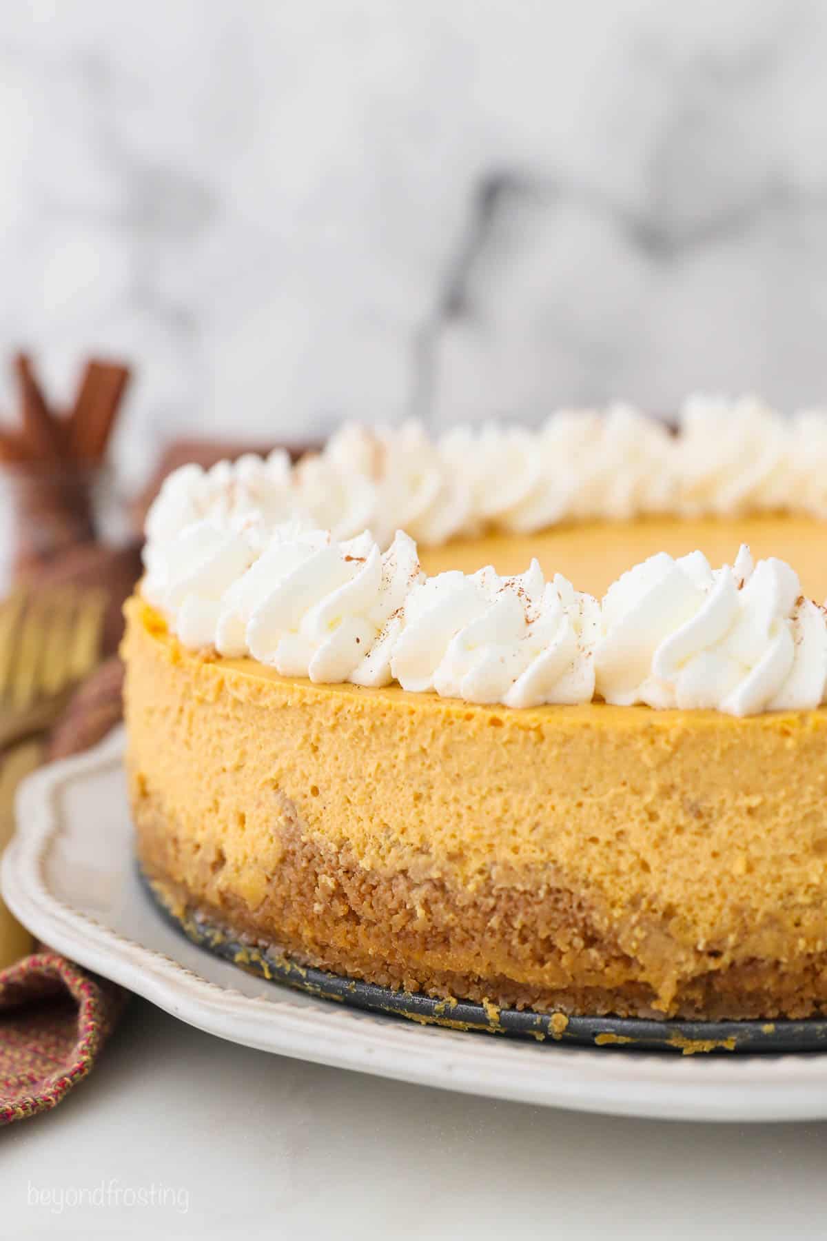 A fall-spiced cheesecake on a serving platter with homemade whipped cream along the top edge