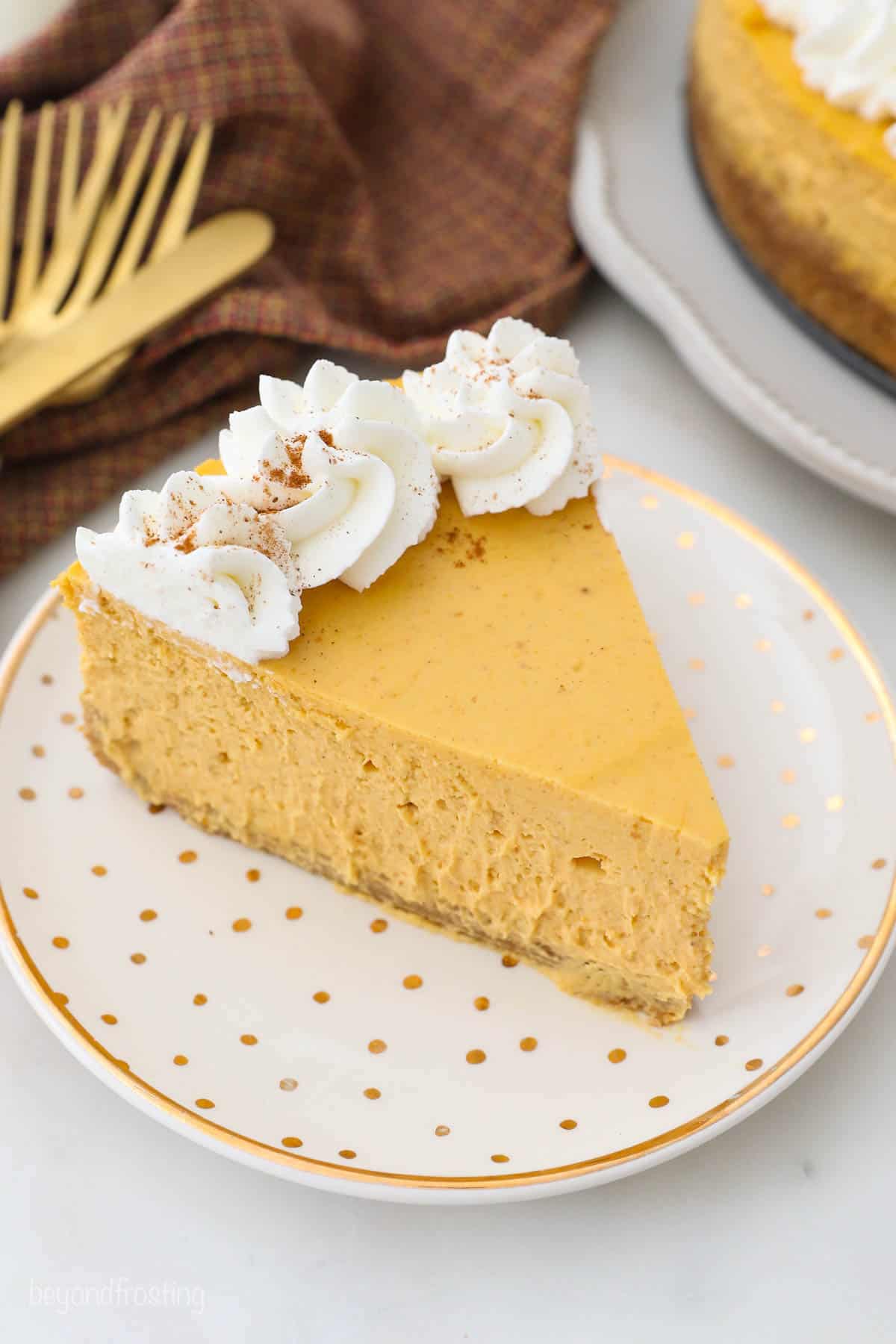 A single piece of pumpkin cheesecake on a white plate with a gold rim and gold speckles