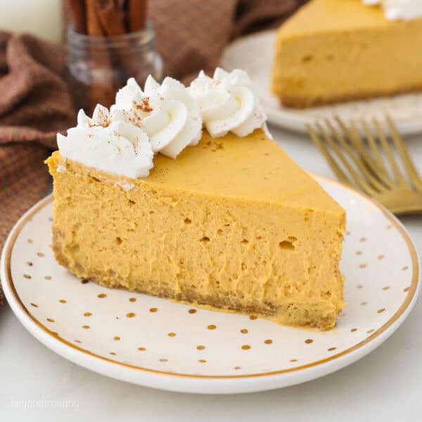 A close-up shot of a slice of pumpkin cheesecake with a second slice on a plate in the background