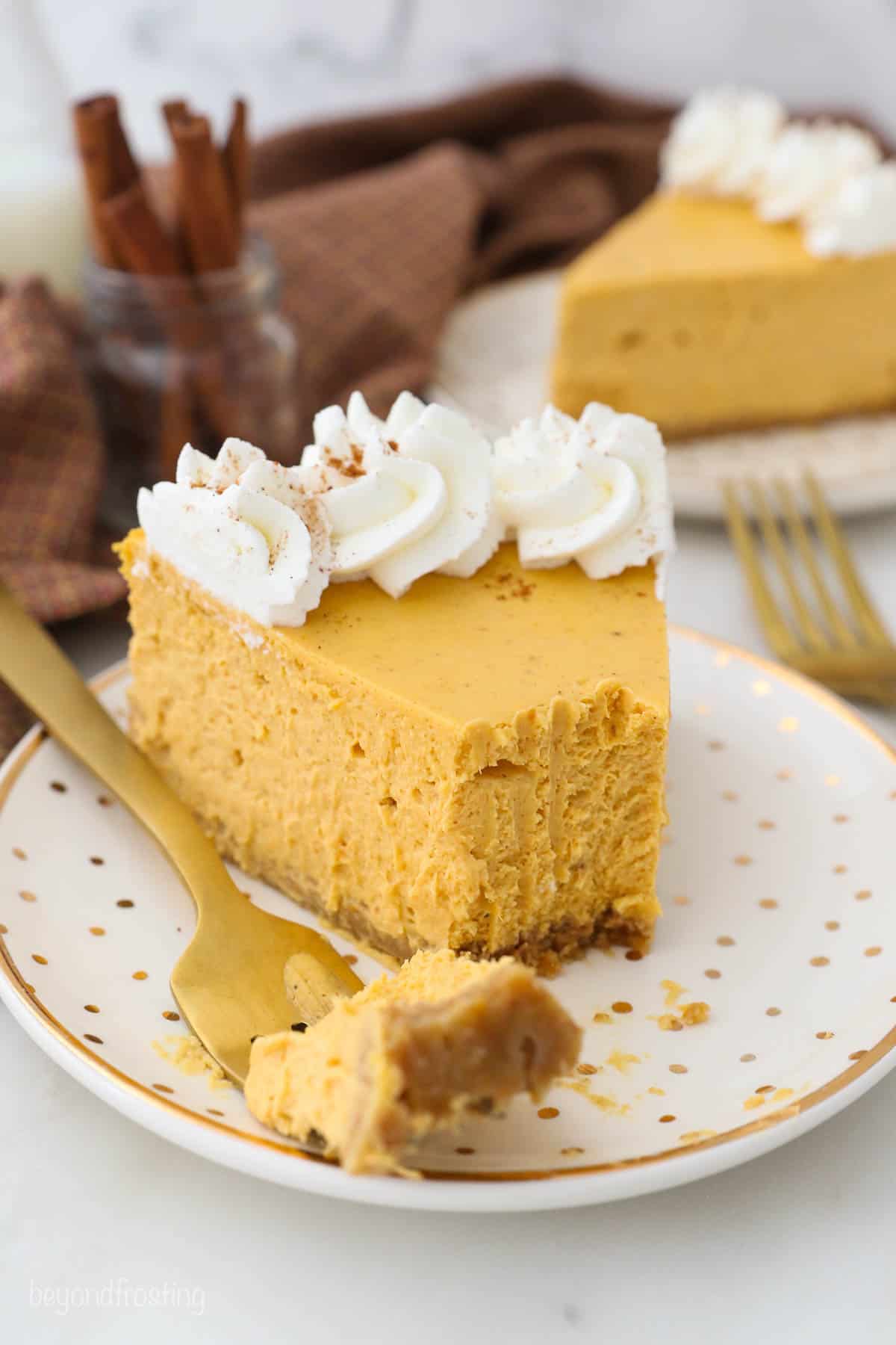 A piece of pumpkin cheesecake on a plate with one bite on a golden fork
