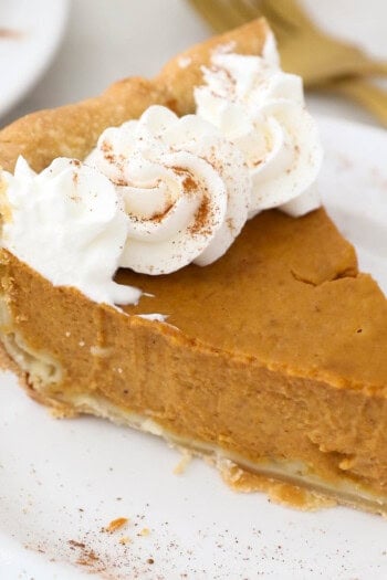 A slice of homemade pumpkin pie topped with whipped cream on a white plate.