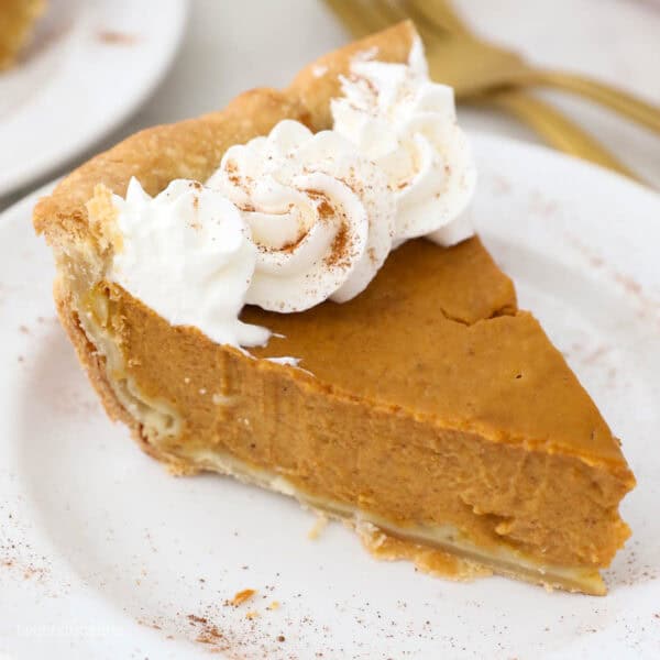 a slice of pumpkin pie topped with whipped cream on a white plate