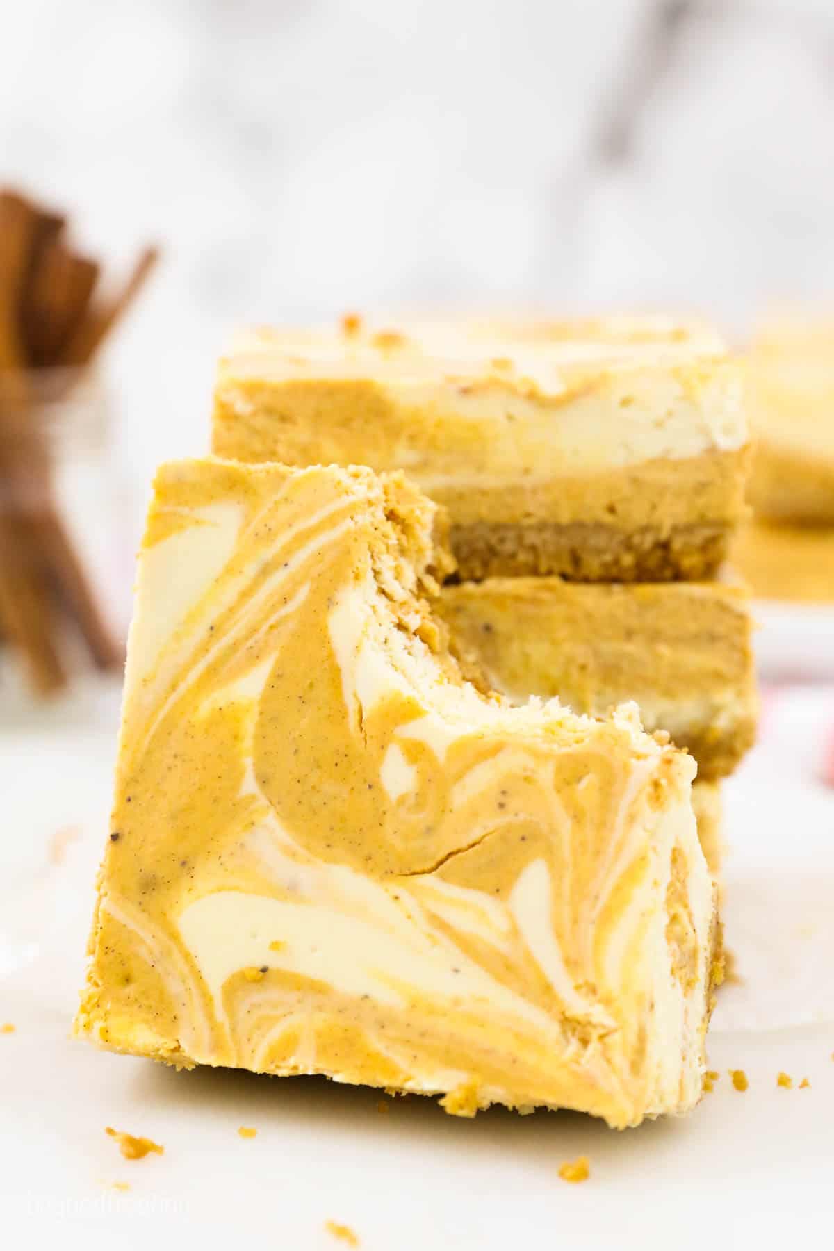 A pumpkin cheesecake bar with a bite missing, leaning up against a stack of bars