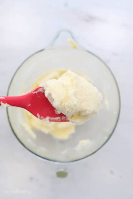 a red spatula with creamed butter and sugar being held over top of a glass mixing bowl