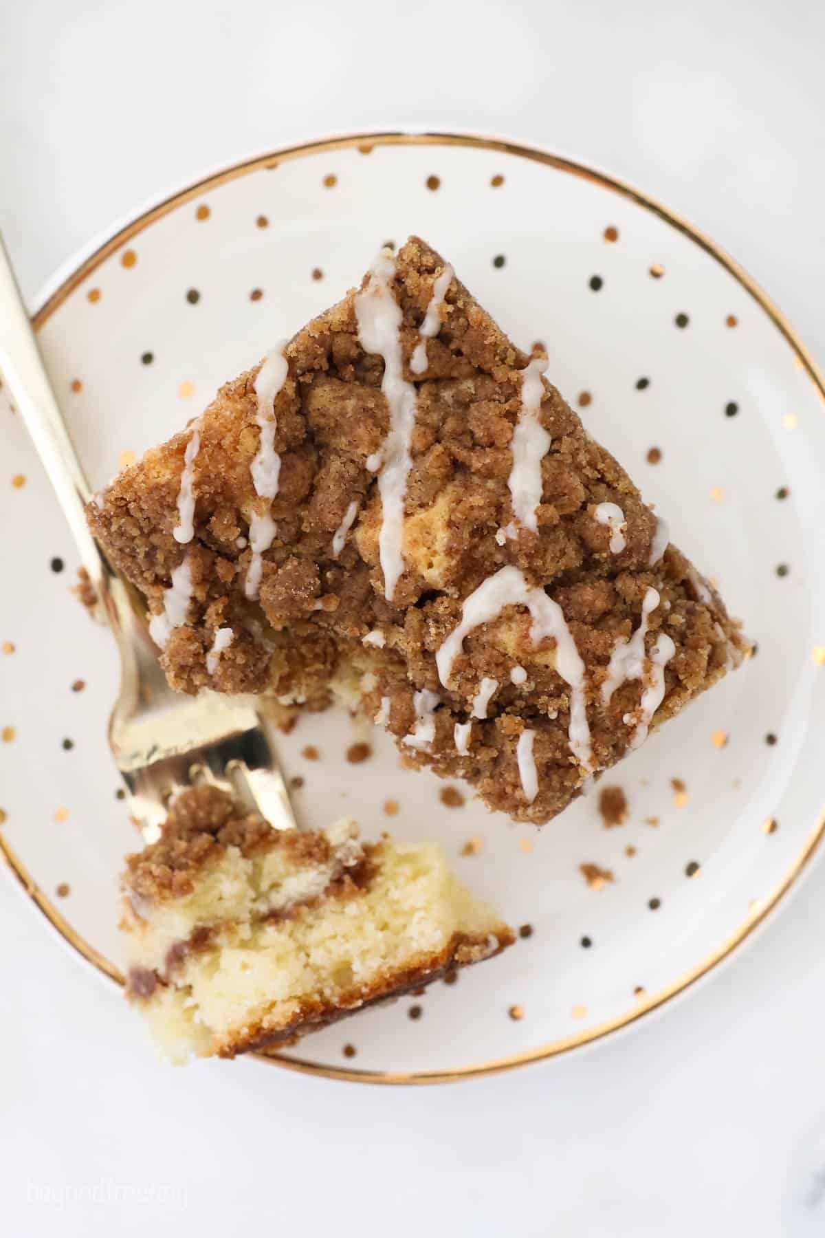 This classic coffee cake recipe is a thick, moist sour cream cake with a crumbly, buttery cinnamon streusel. Enjoy a slice with coffee or tea! Overhead view of a slice of sour cream coffee cake with a forkful missing on a plate.