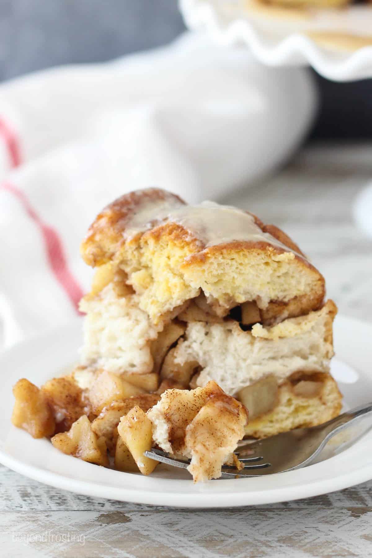 A serving of apple pie pull apart bread on a plate with a fork and a kitchen towel in the background