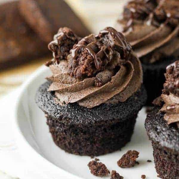 a close up of a chocolate cupcake topped with chocolate frosting, brownie chunks and hot fudge