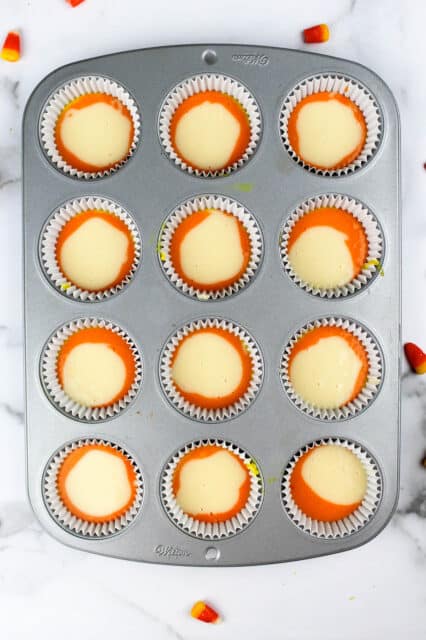 a cupcake pan filled with orange and white batter