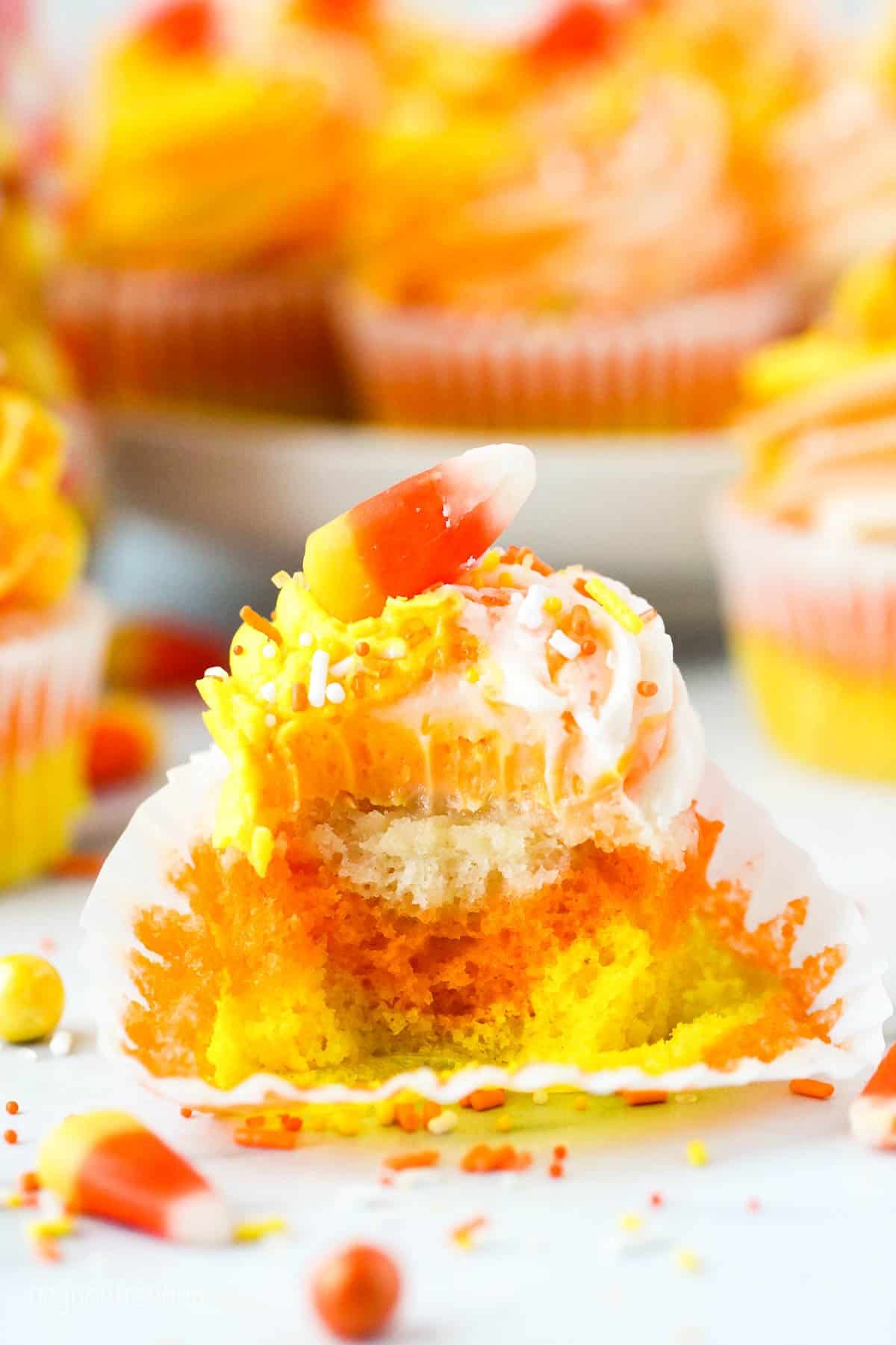 A yellow, orange and white cupcake with a bite taken out of it