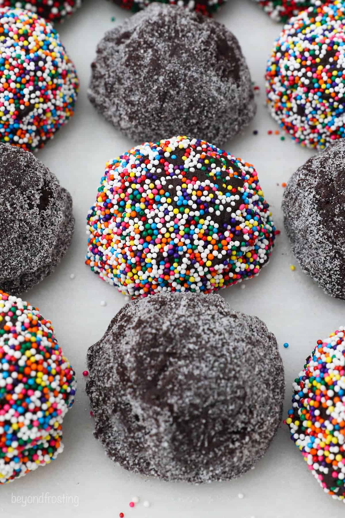 Balls of dough on a countertop with alternating coatings of sprinkles and granulated sugar