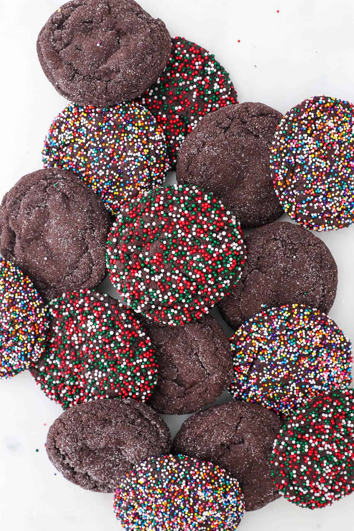 A pile of chocolate sugar cookies with various decorations on top of a white countertop