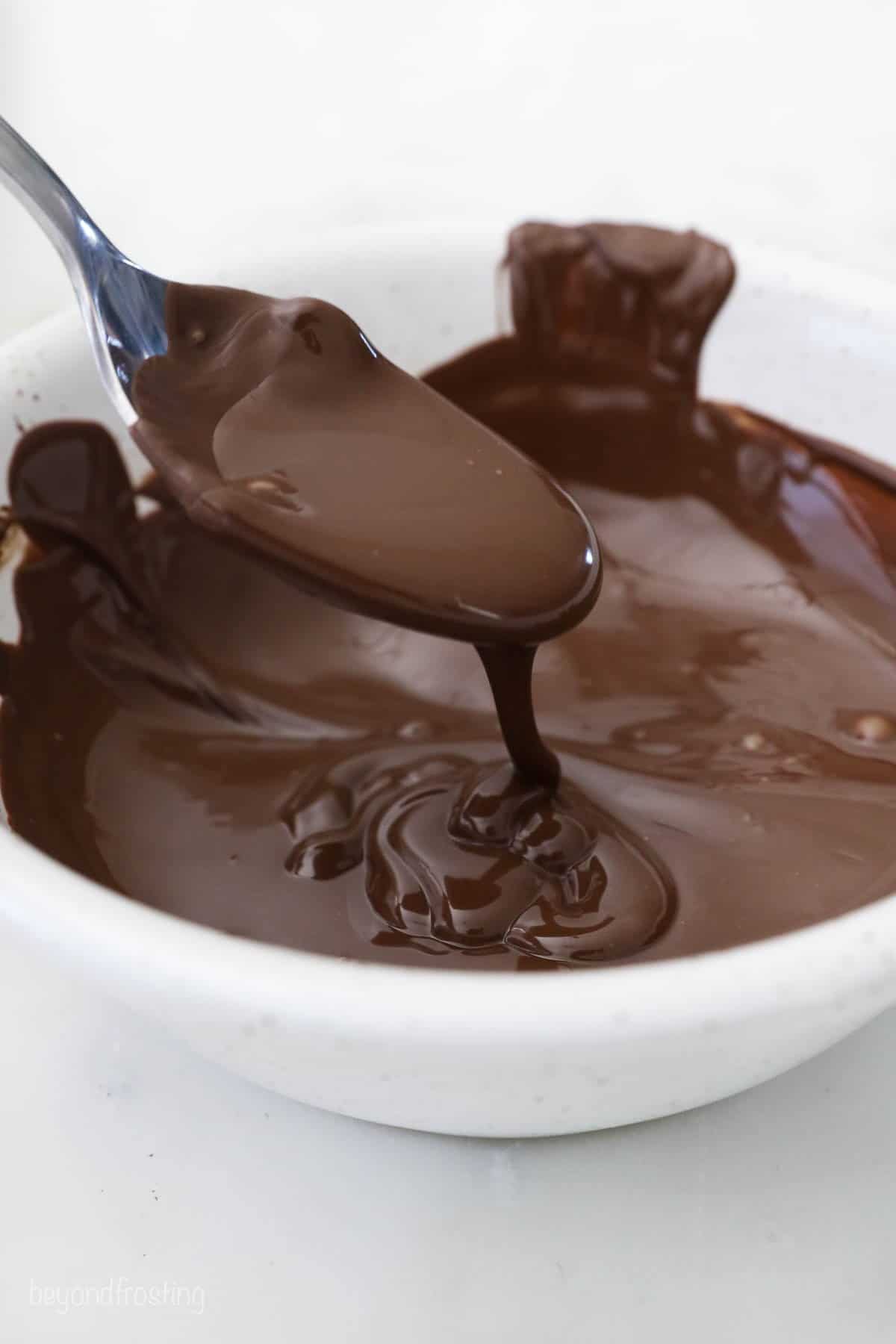 Melted chocolate in a white bowl with a metal spoon scooping some out