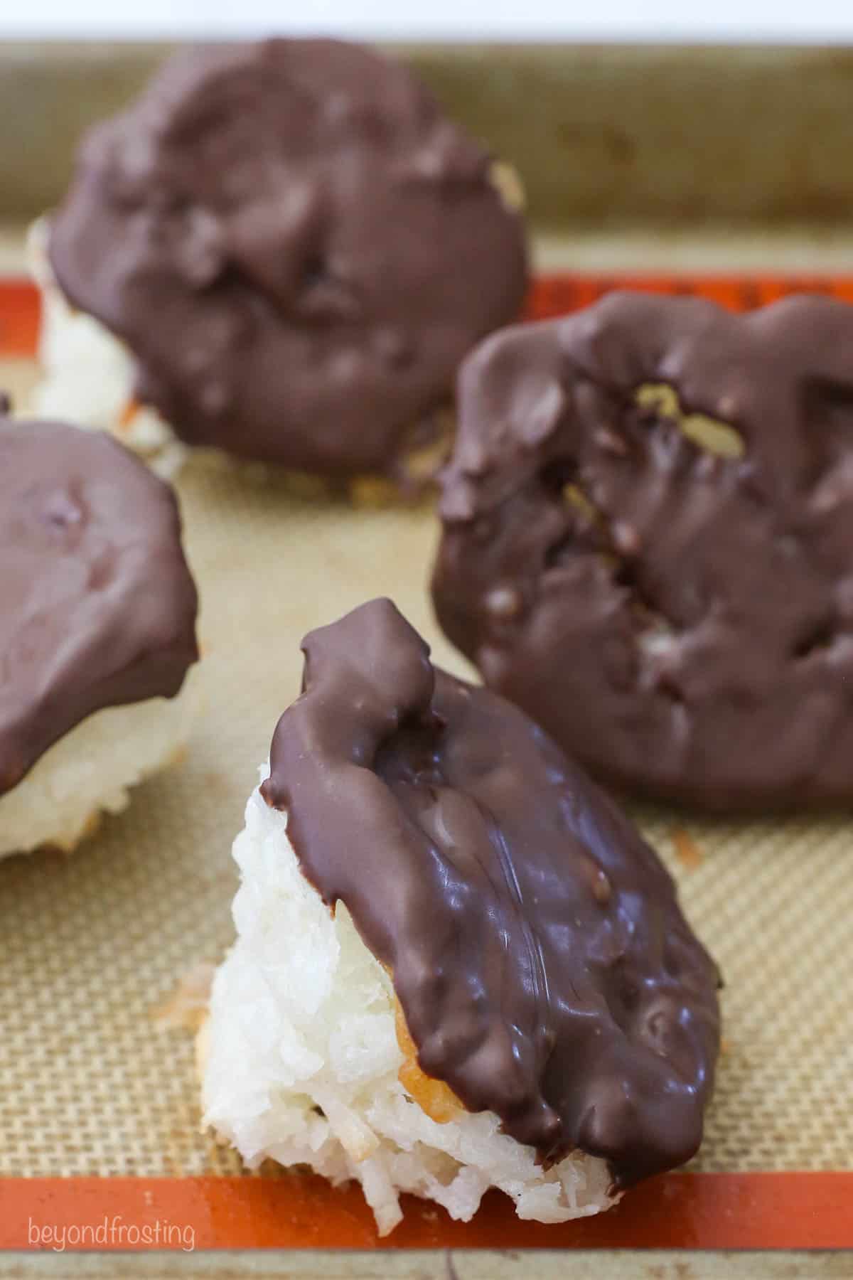 Chocolate-dipped macaroons laying on their sides on top of a silicone-lined baking sheet