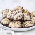 A pile of chocolate coconut macaroons with golden brown edges on a rimmed dessert plate