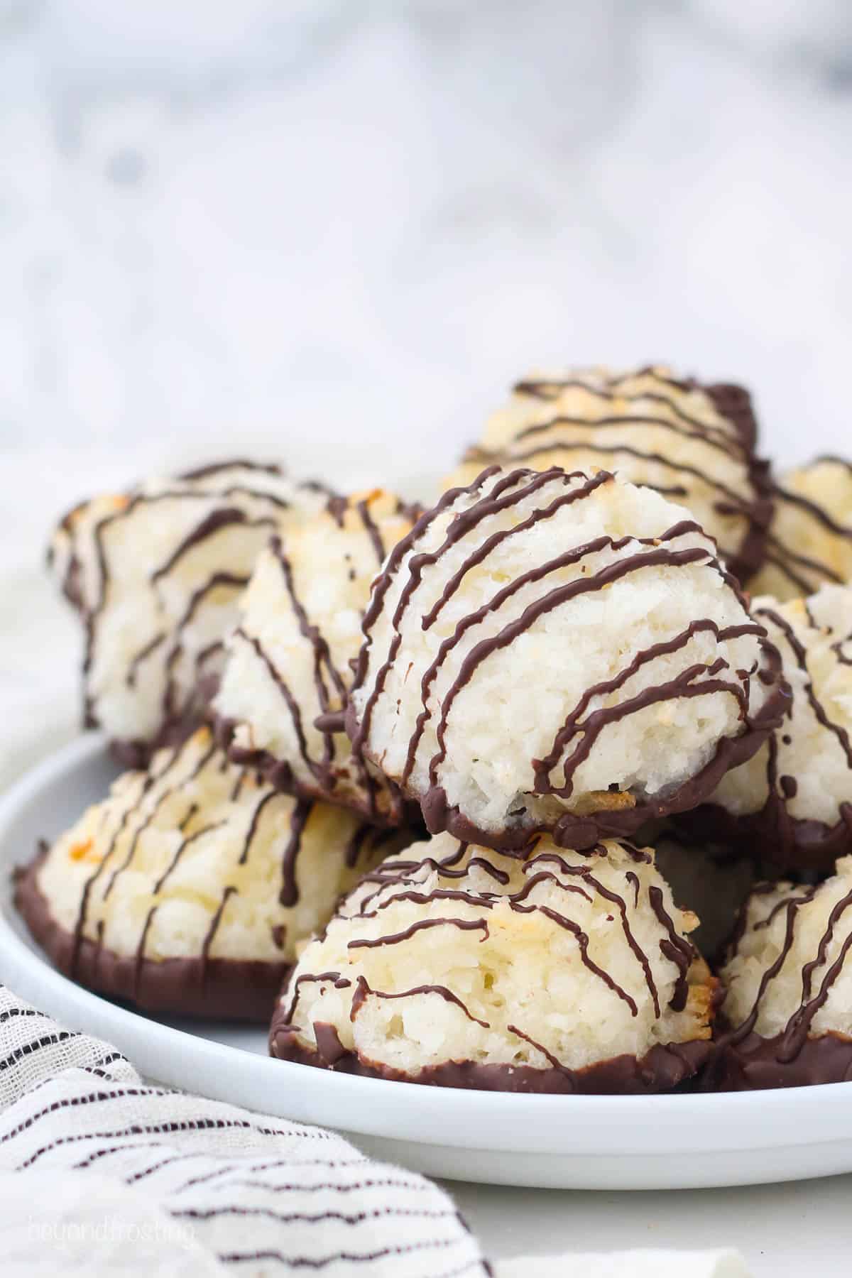 Coconut cookies with a chocolate drizzle piled onto a white plate