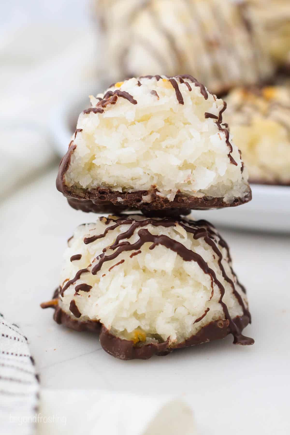 Two chocolate coconut macaroons stacked on top of one another with a bite taken out of the top one