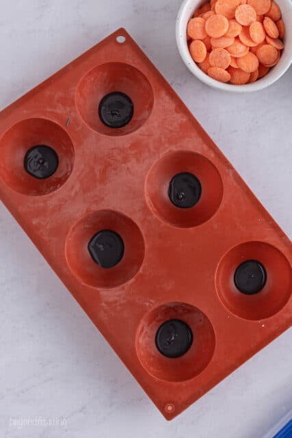 a red silicone mold with 6 cavities filled with black candy melts