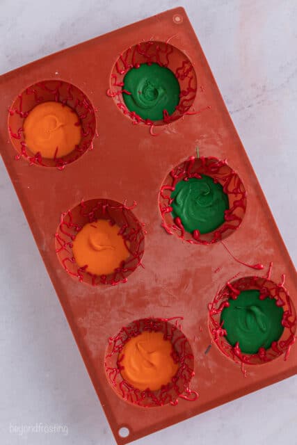 a red silicone mold with 6 cavities filled with red, green and orange candy melts