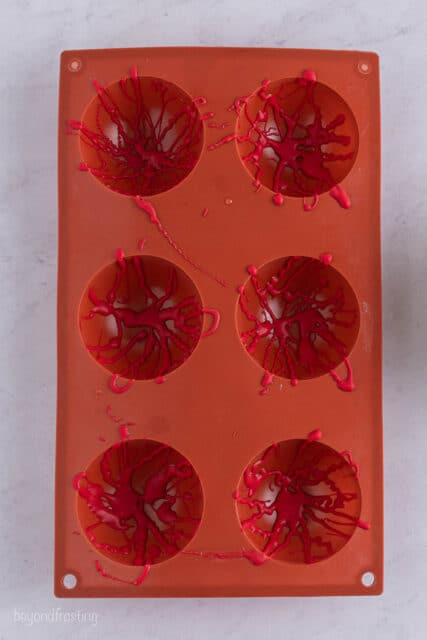 a red silicone mold with 6 cavities drizzled with red candy melts