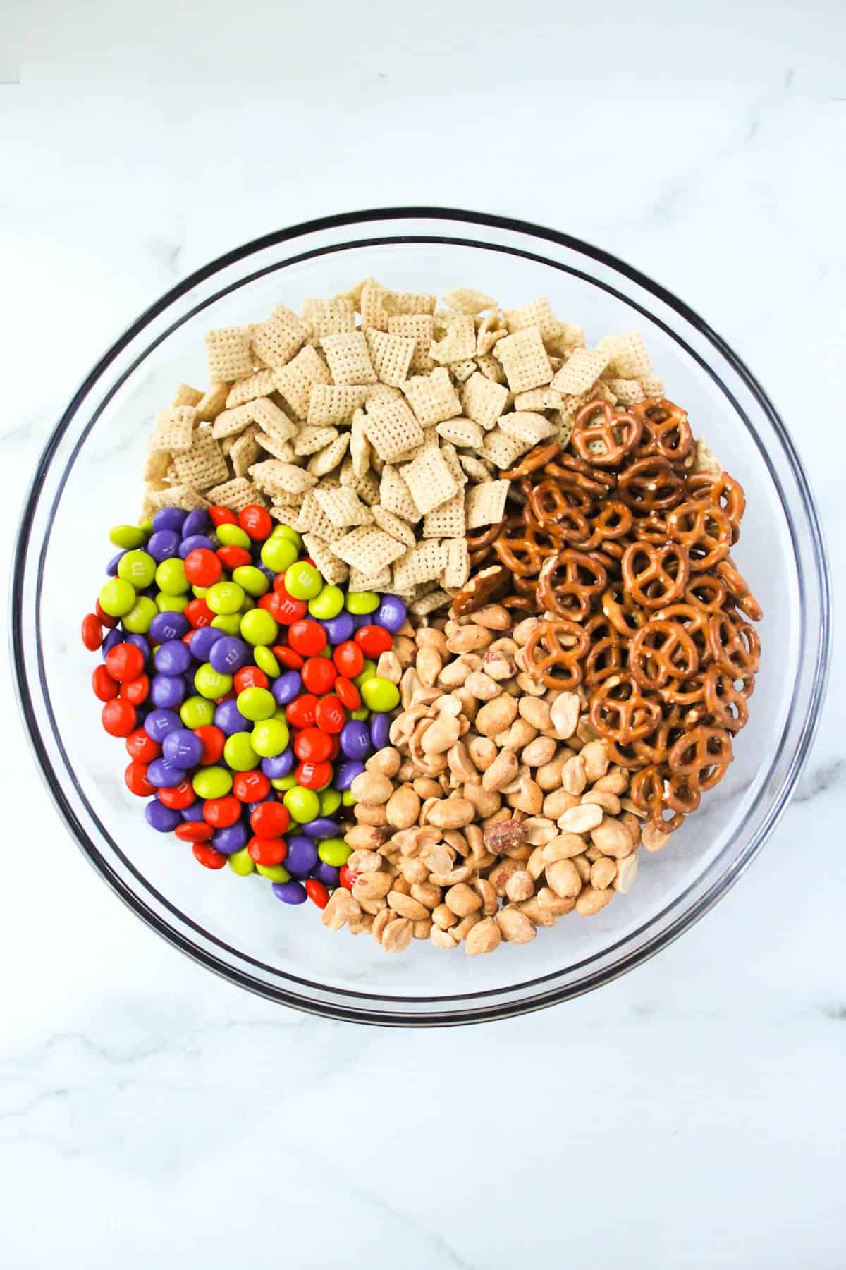 a glass mixing bowl with chex ceral, cereal, peanuts and M&Ms