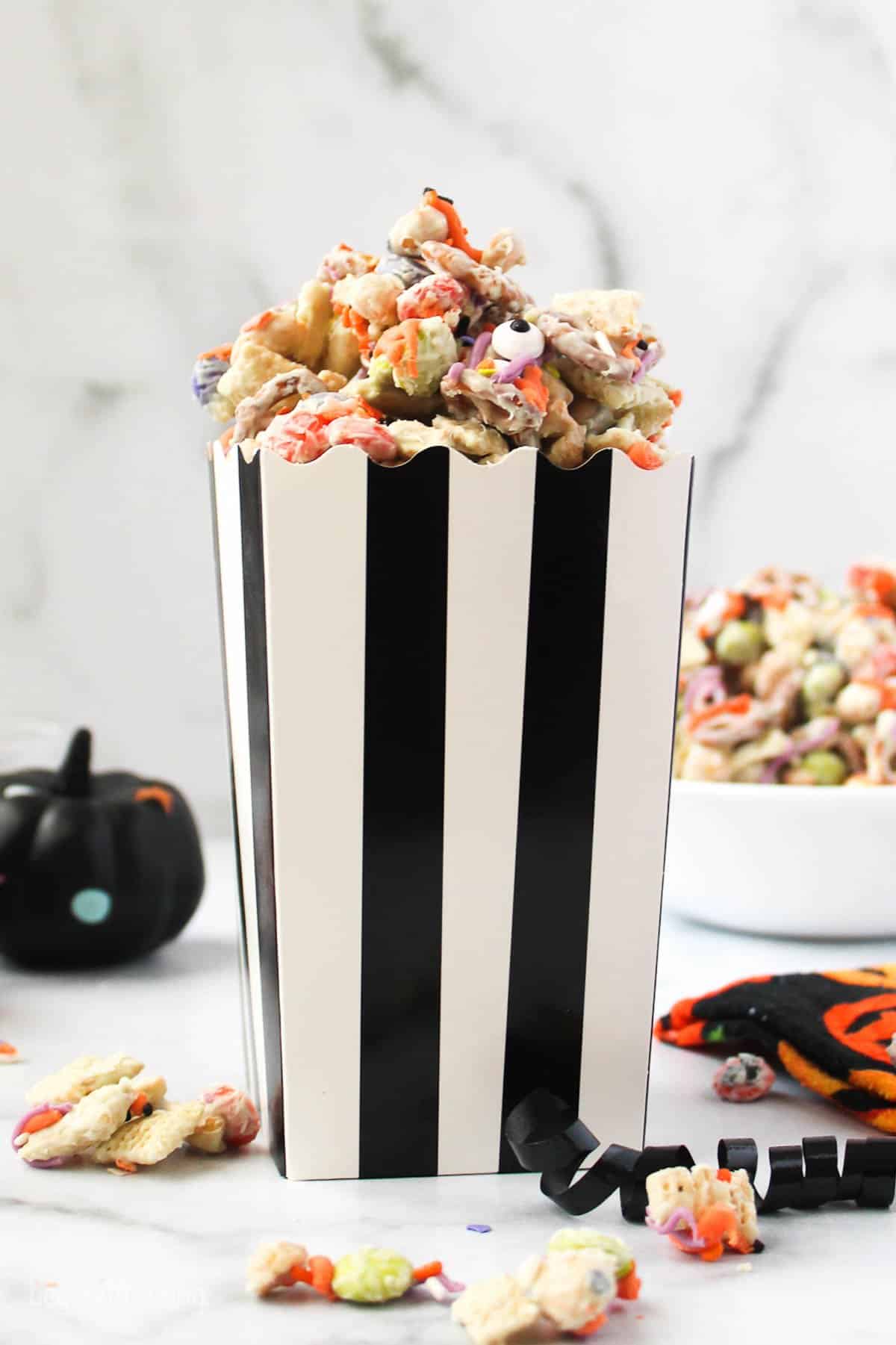 A black and white striped container filled with monster munch Halloween snack mix.