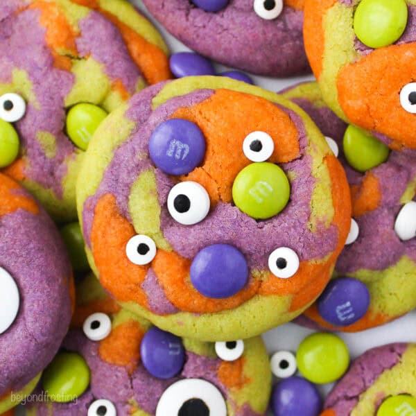 close up shot of halloween monster cookie- tye dye orange, purple and green with M&Ms and candy eyes