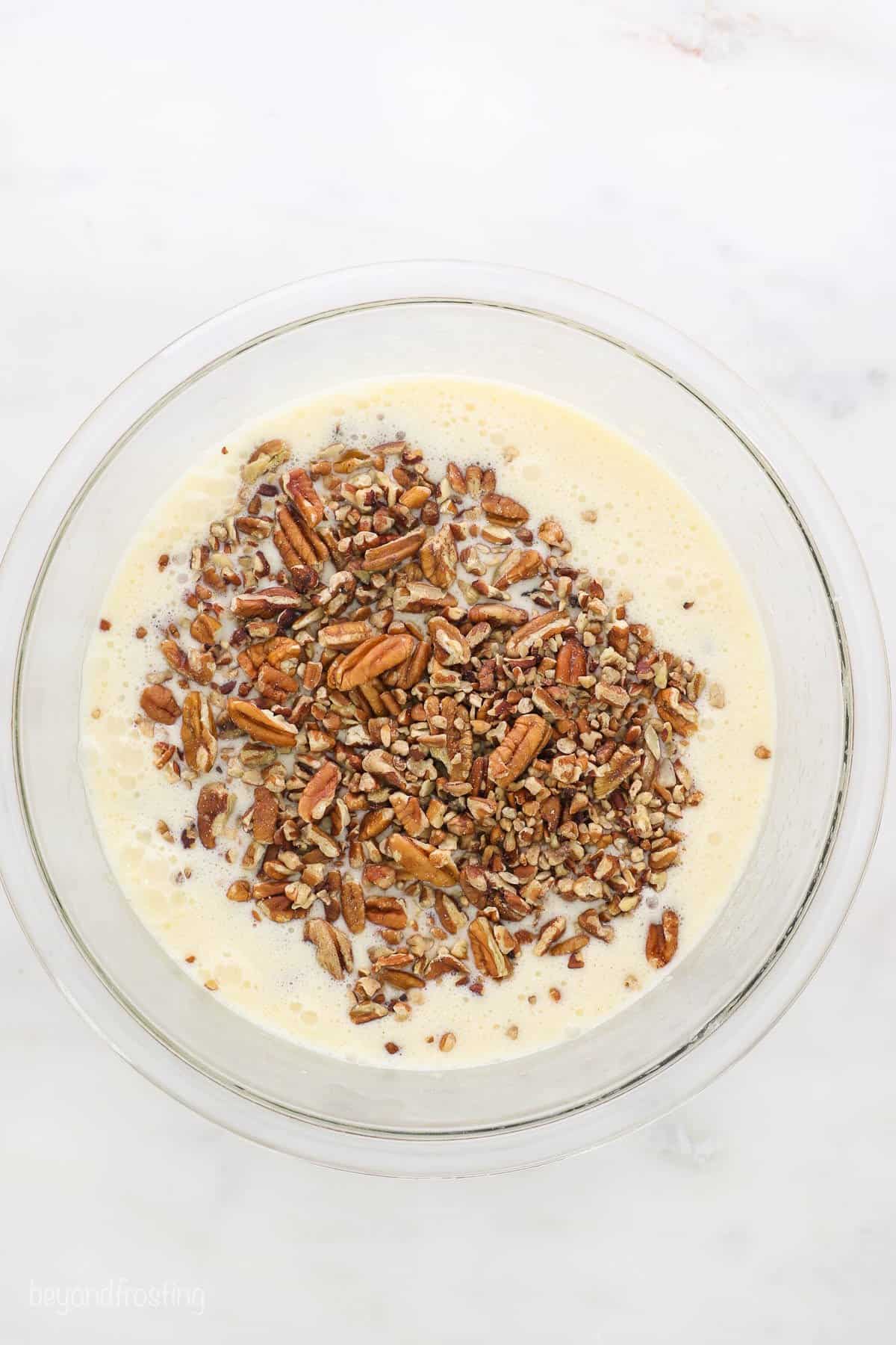 A glass bowl full of the combined filling with chopped pecans poured on top