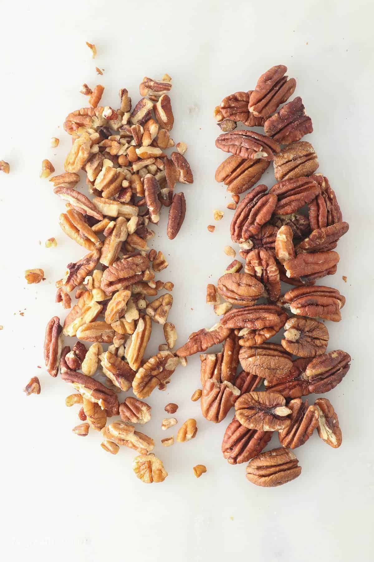 Chopped pecans on a white surface beside whole pecans