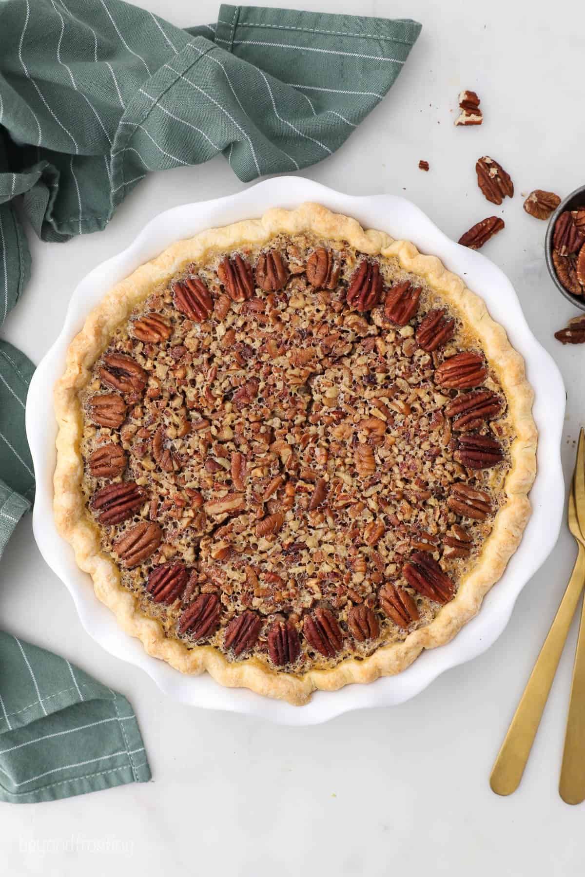 A Kahlua pecan pie in a pie plate on a countertop beside a kitchen towel