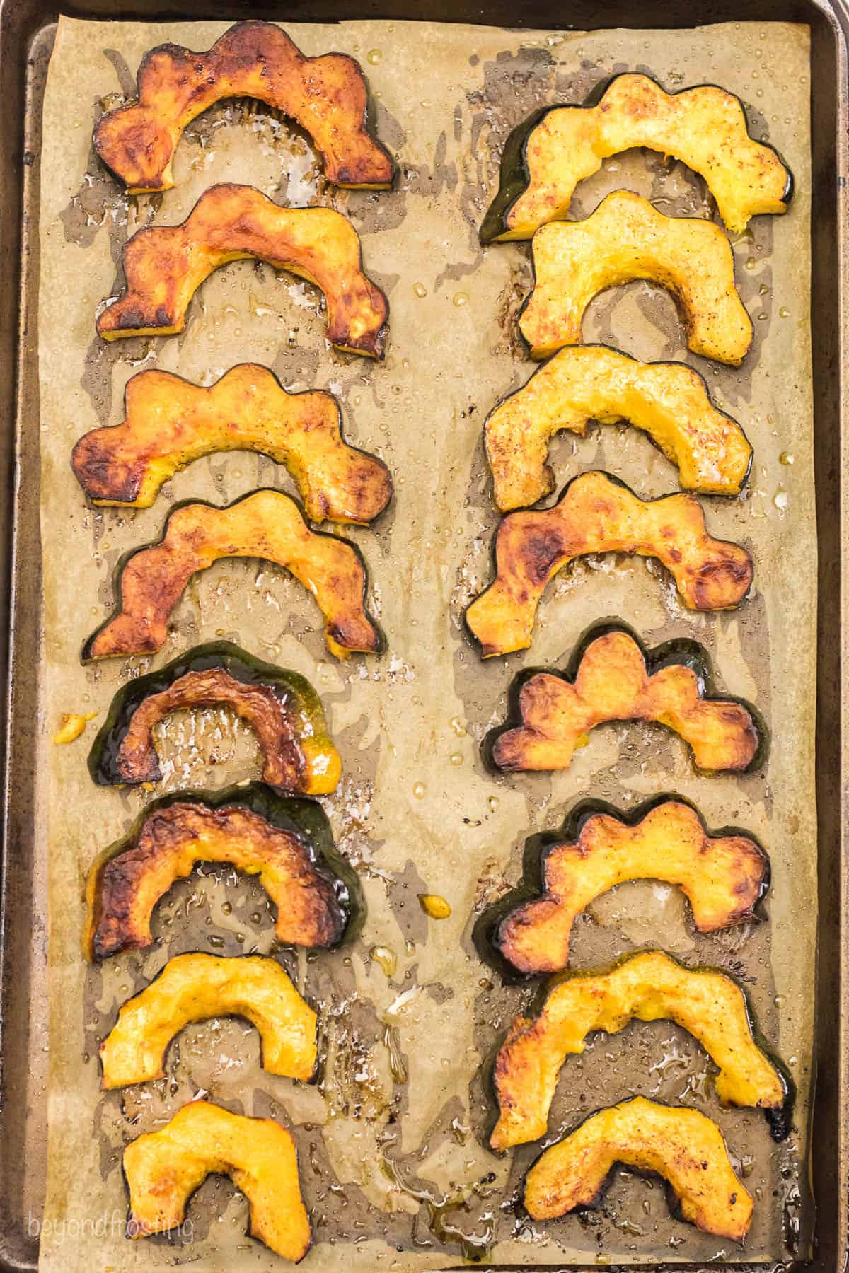 Freshly roasted acorn squash slices on a metal baking sheet lined with parchment paper
