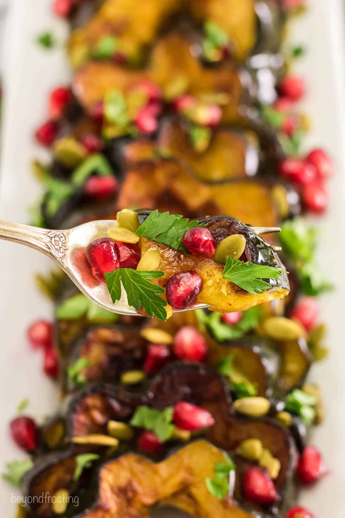 A spoon holding a bite of baked acorn squash, pumpkin seeds and pomegranate arils
