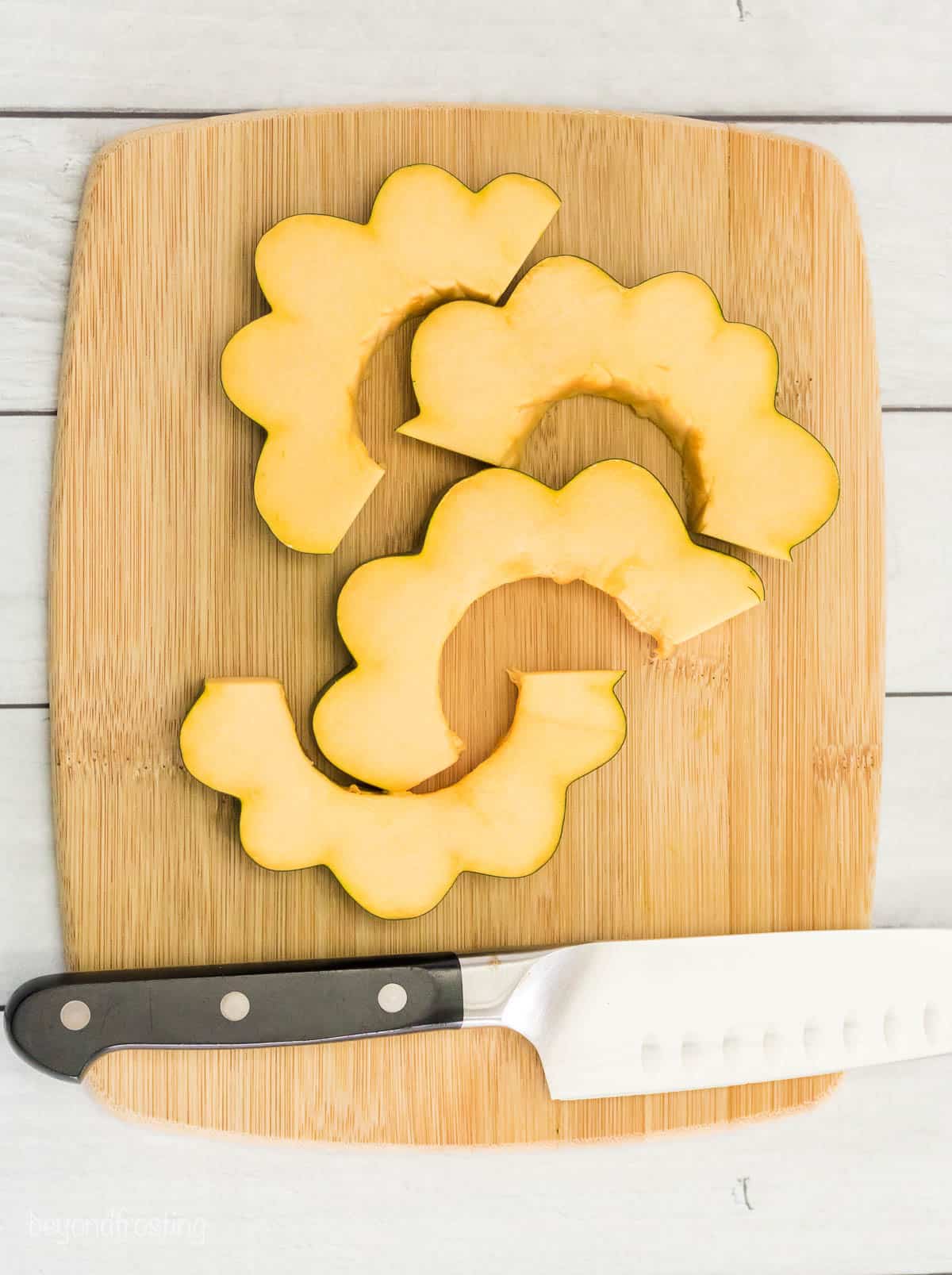 Four squash slices on a wooden cutting board with a sharp chef's knife