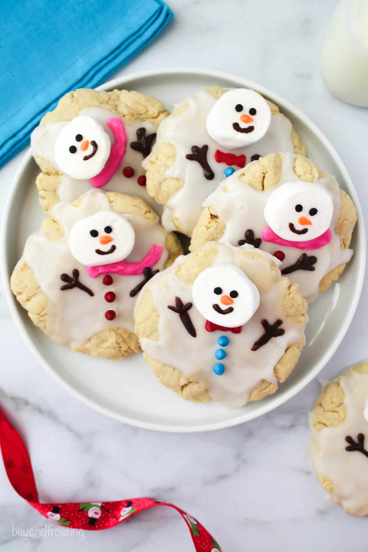 overhead of melted snowman cookies on a plate next to a red ribbon