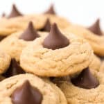A close up of a batch of Peanut Butter Blossoms with some stacked on top of each other.