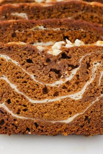 A close up shot of sliced pumpkin bread with swirls of cream cheese filling