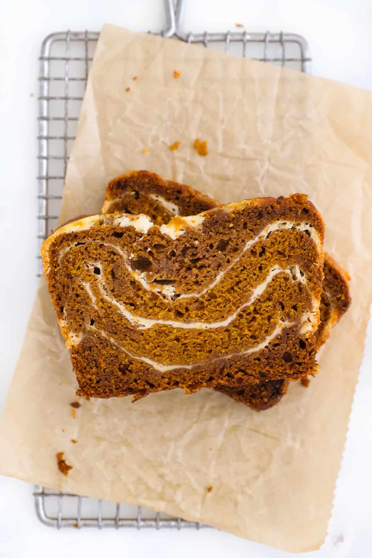 Two sliced of sliced pumpkin bread on a wire rack with brown parchment paper