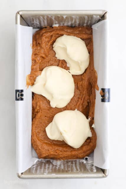 overhead shot of a loaf pan with pumpkin bread swirled with cream cheese filling