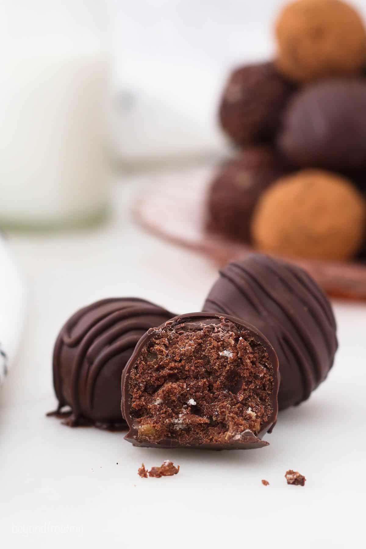 A chocolate rum ball broken in half on a countertop with a glass of milk in the background