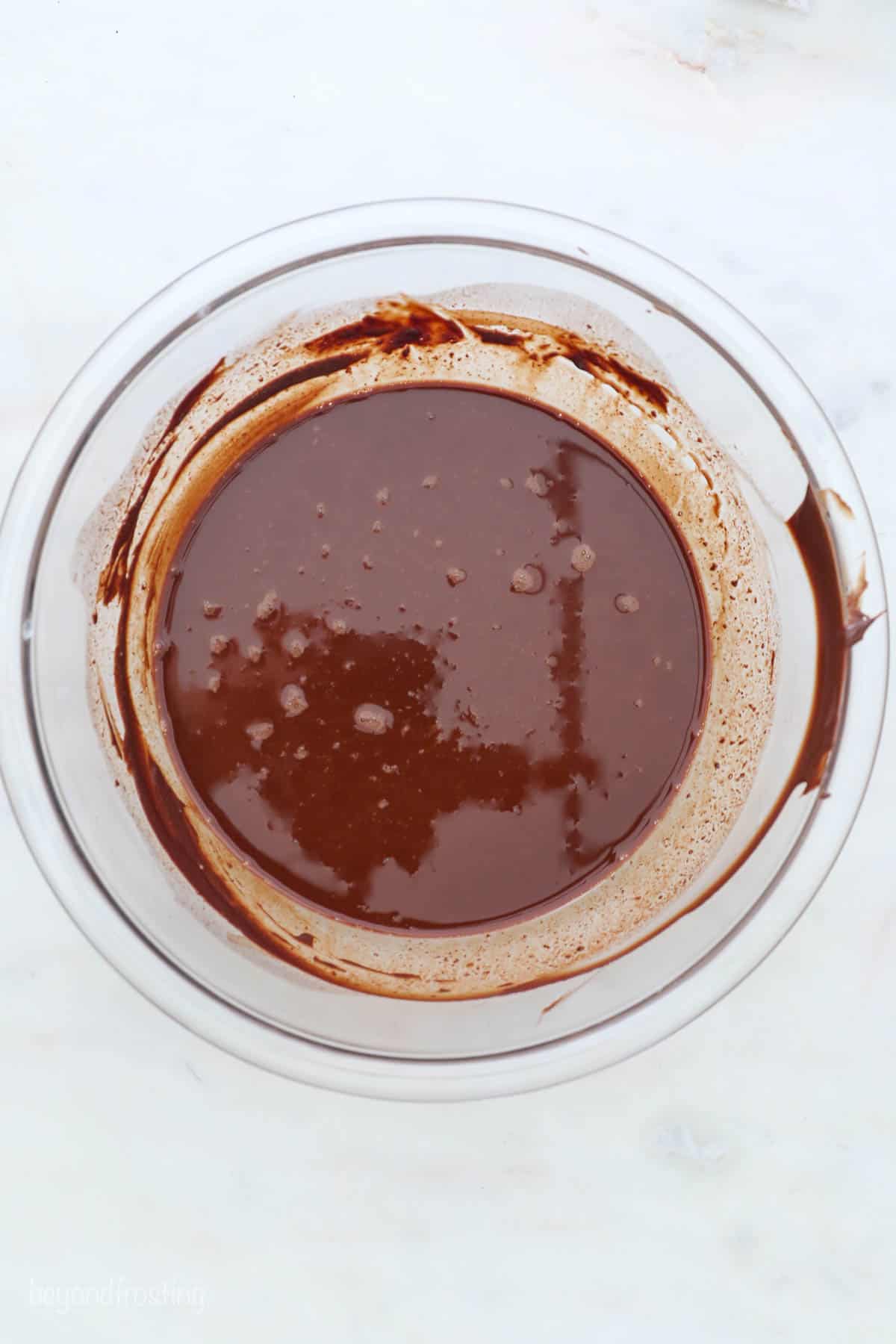 A glass bowl full of melted dark chocolate on a white countertop
