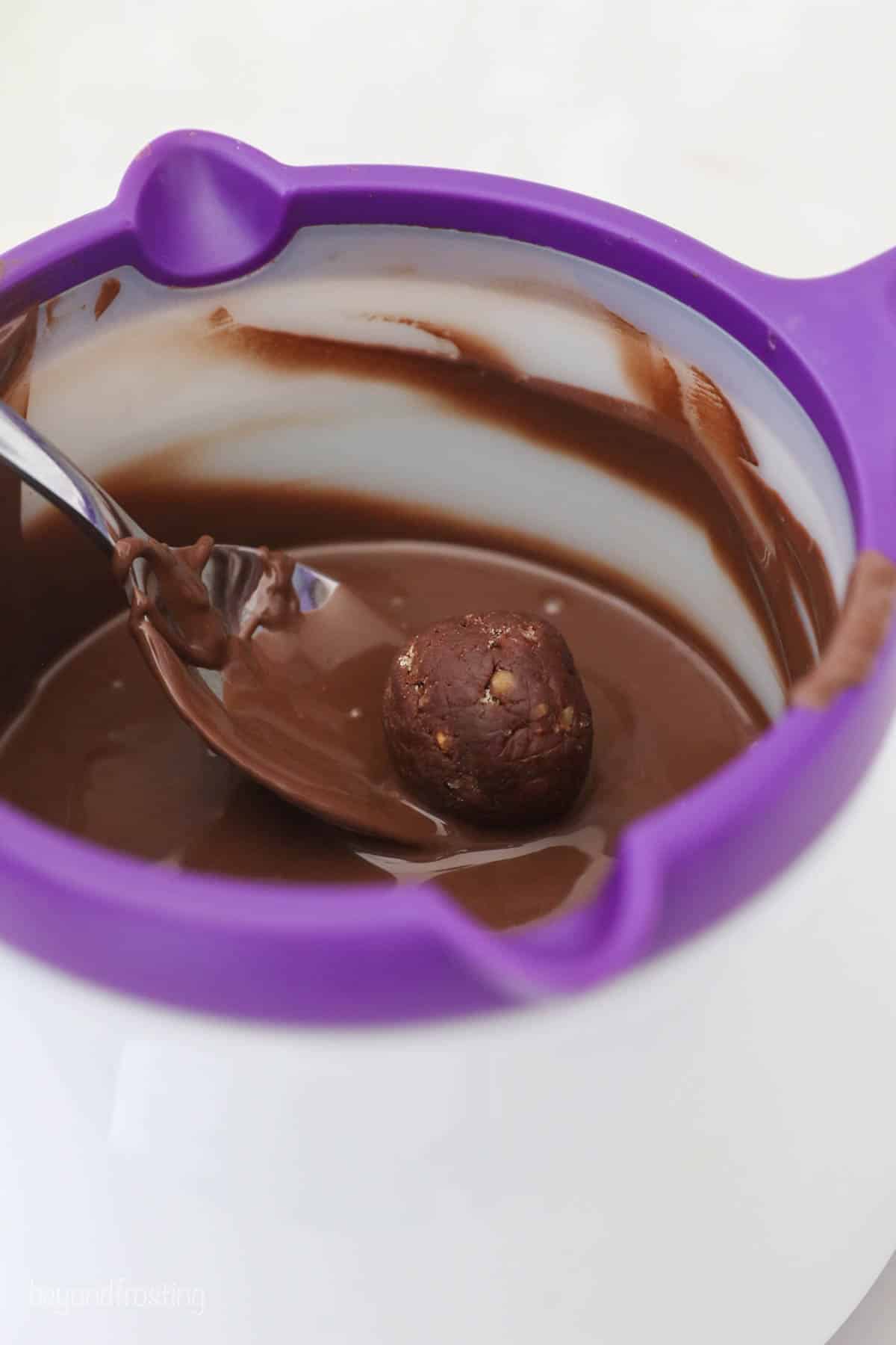 A rum ball being dipped into melted chocolate inside of a Wilton candy melting pot