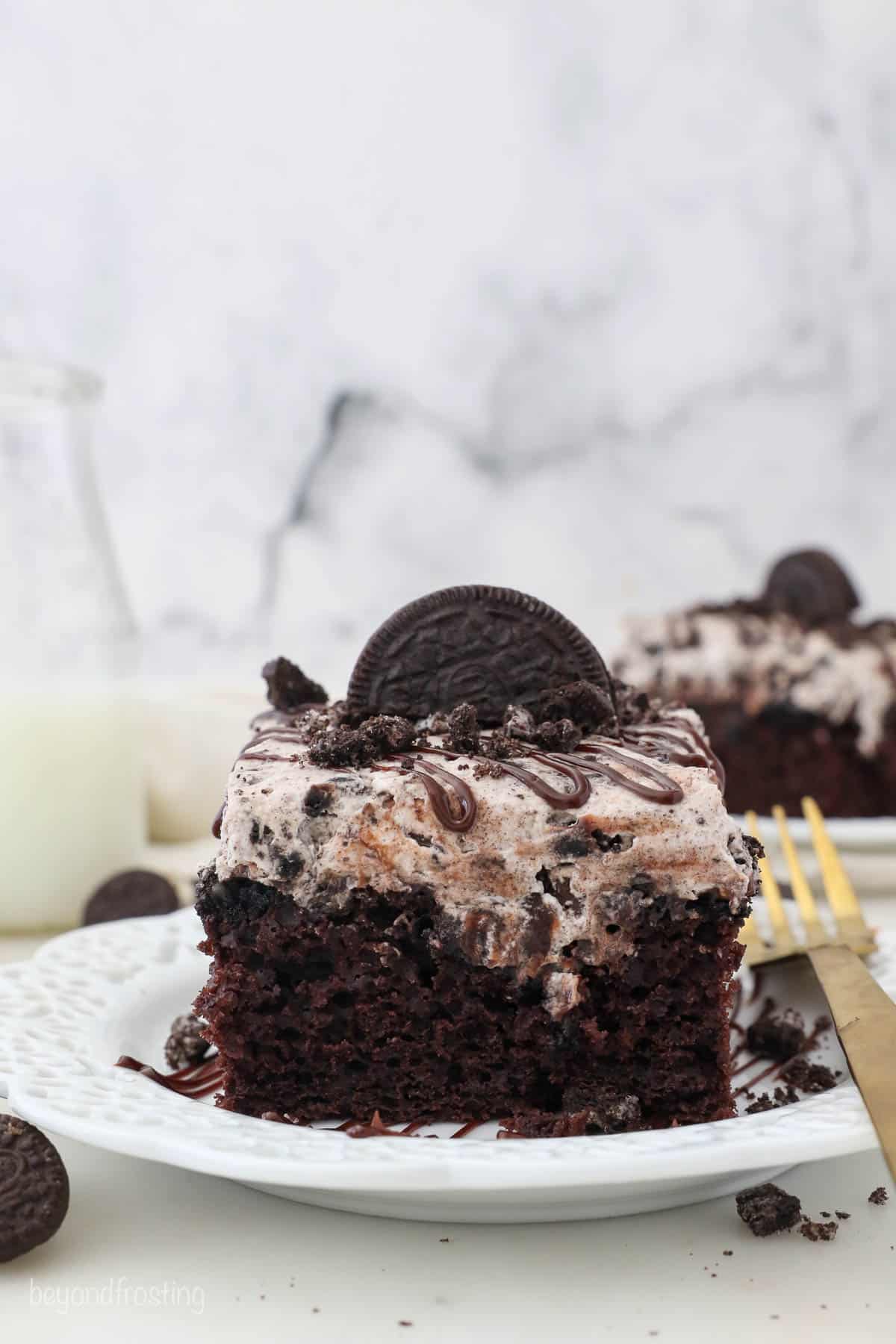 slice of Oreo poke cake topped with an Oreo cookie on a white plate with a gold fork