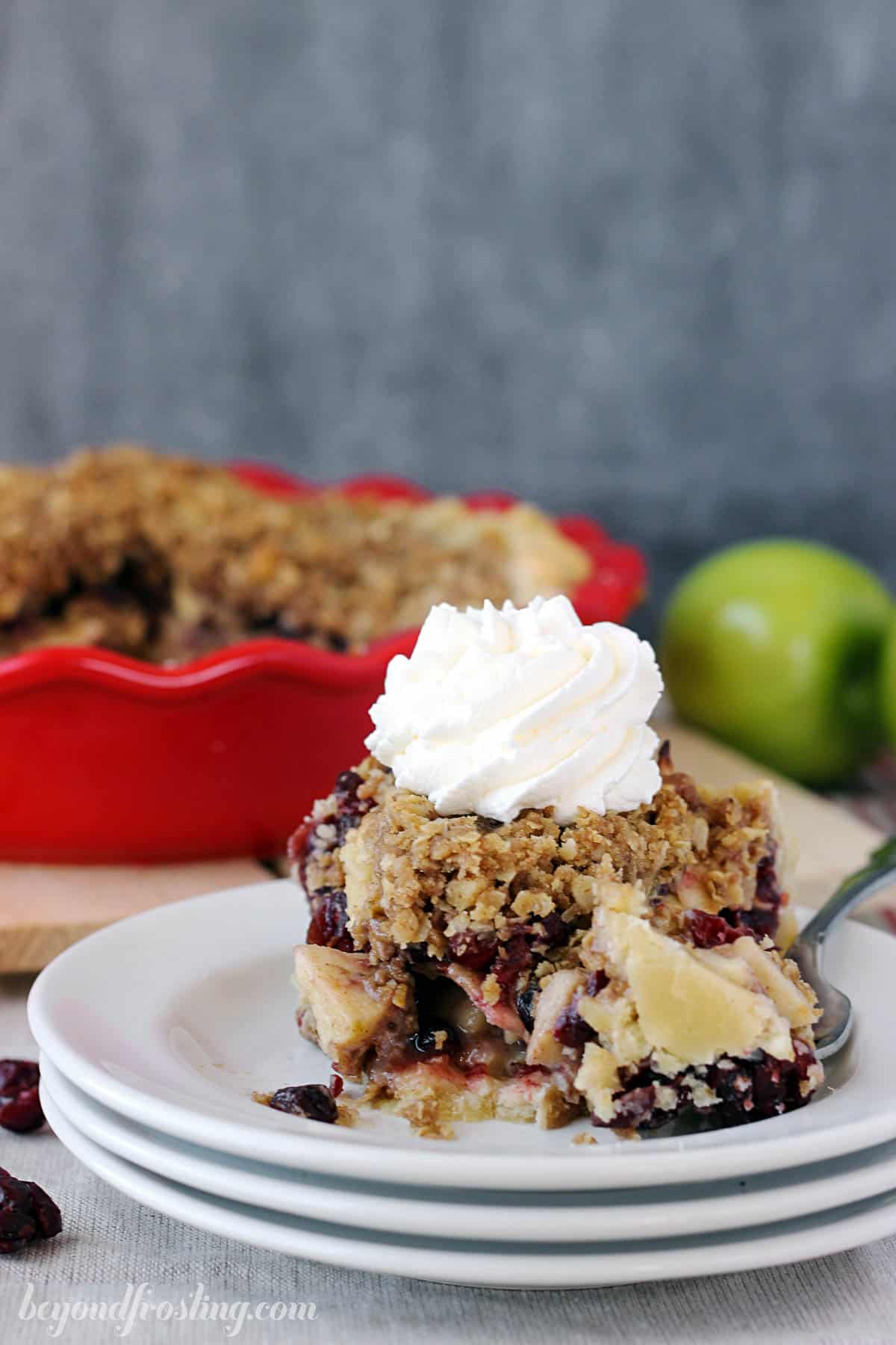 A piece of cranberry apple pie on top of a stack of three plates with one bite on a fork