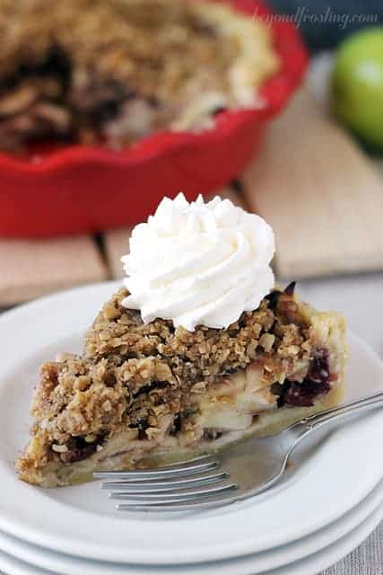 A slice of cranberry apple pie with a dollop of homemade whipped cream on top