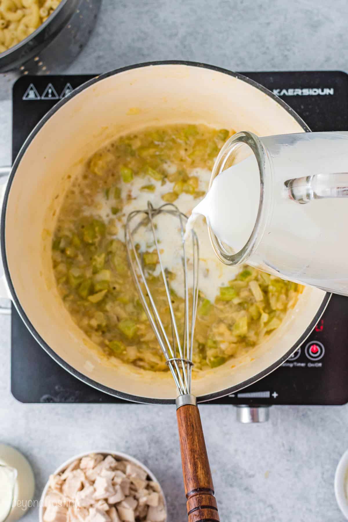 Whole milk being poured into a saucepan containing butter, onion, garlic, celery and flour
