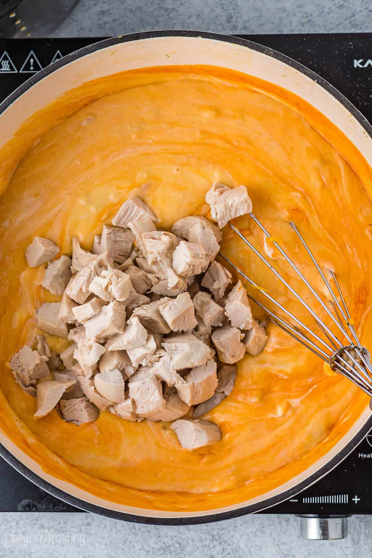 Chopped chicken being mixed into a saucepan full of cheesy buffalo sauce