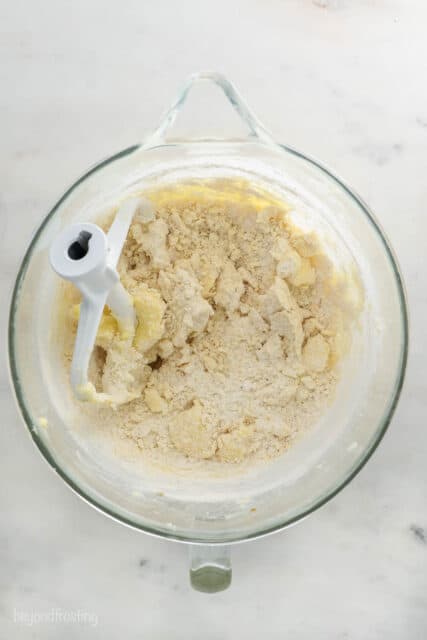 The in-progress cookie dough in a large glass beaker after the dry ingredients have been poured in