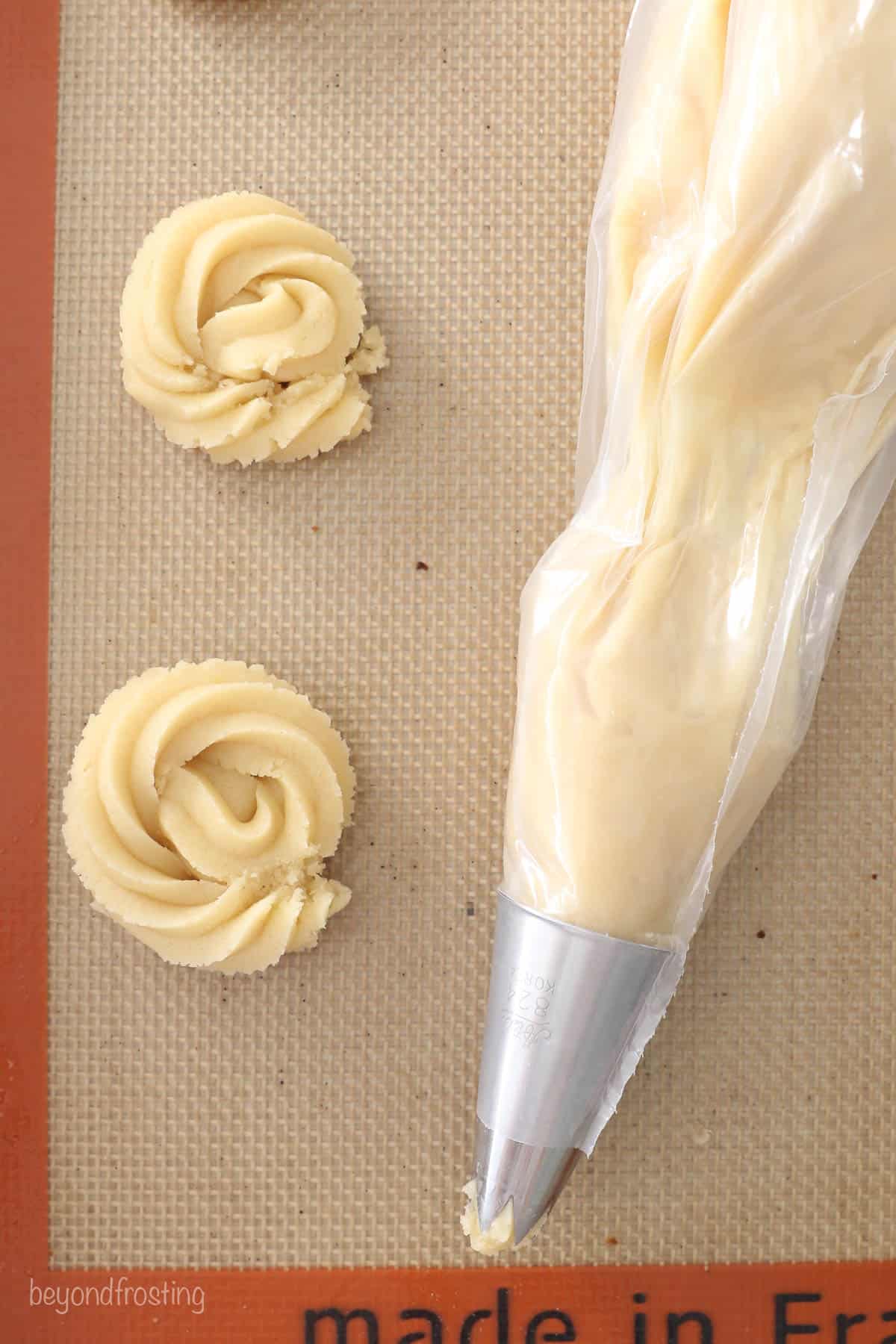 Two swirls of cookie dough beside a double-bagged piping bag on a baking sheet lined with a silicone mat